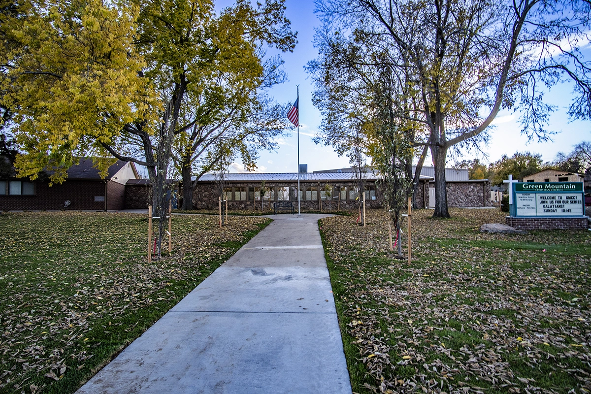 The front walk way to Green Mountain Christian Church, surrounded with trees and with the American flag near the building.
